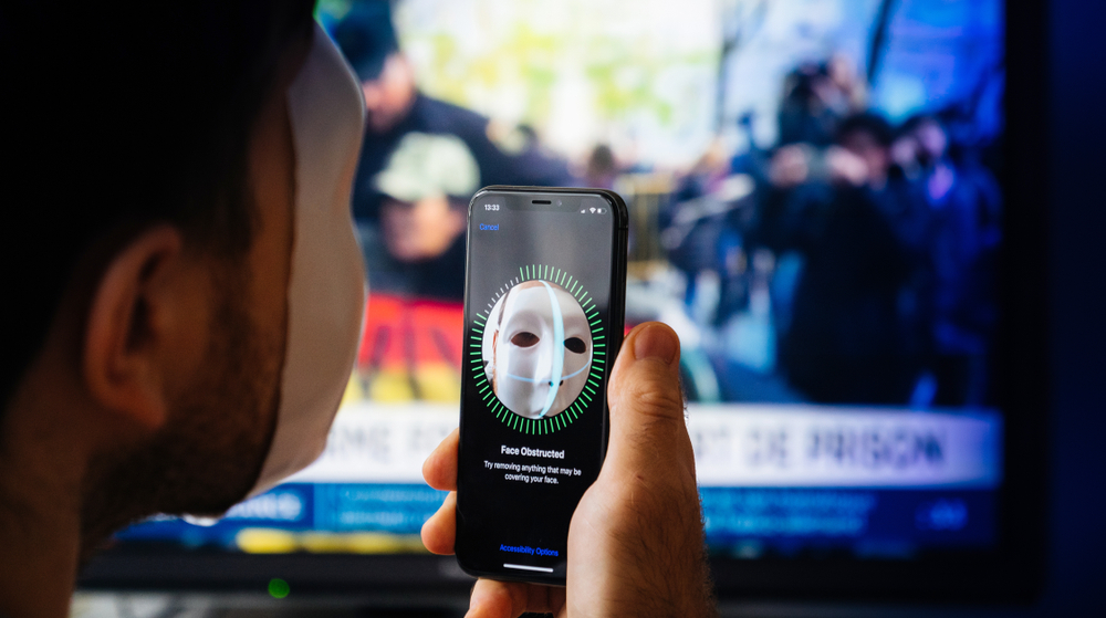Paris, France - Nov 10. 2017: Face Obstructed message on display of new Apple iPhone XS Pro with Face ID virtual facial recognition function with anonymous hacker data monitor in the background