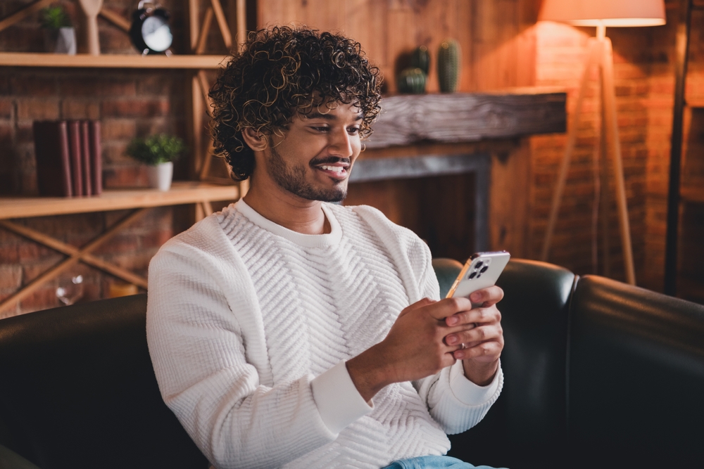 Photo of handsome good mood guy wear white sweatshirt chatting apple samsung iphone device indoors room home house