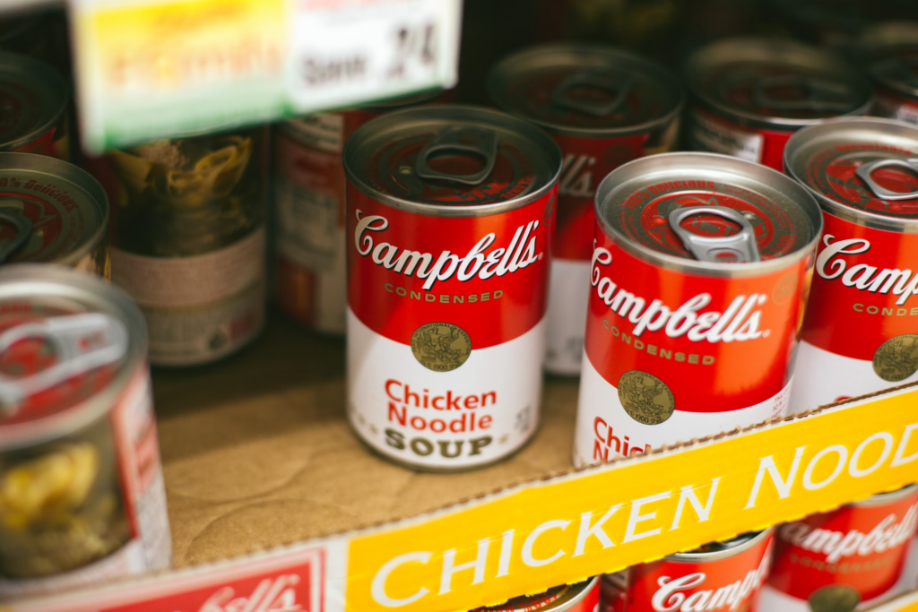 A store shelf stocked with various canned soups, emphasizing their high sodium content, which can contribute to high blood pressure and other health risks for individuals over 60.