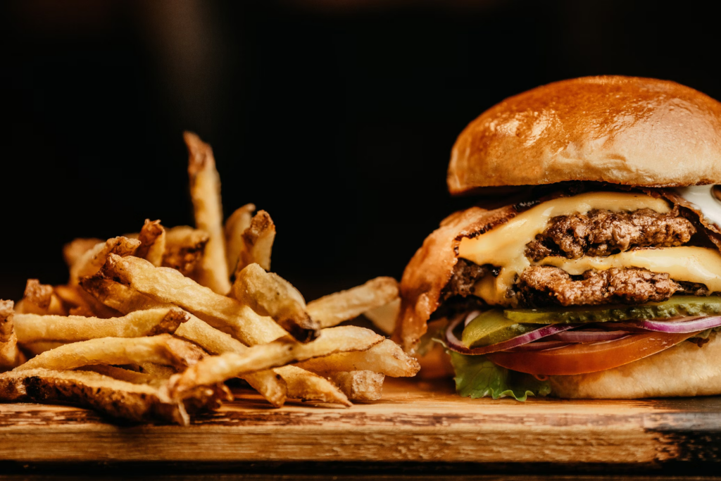 A hamburger and french fries displayed on a wooden cutting board, emphasizing the appeal of fried foods while highlighting their high fat and calorie content, which can pose health risks for people over 60.