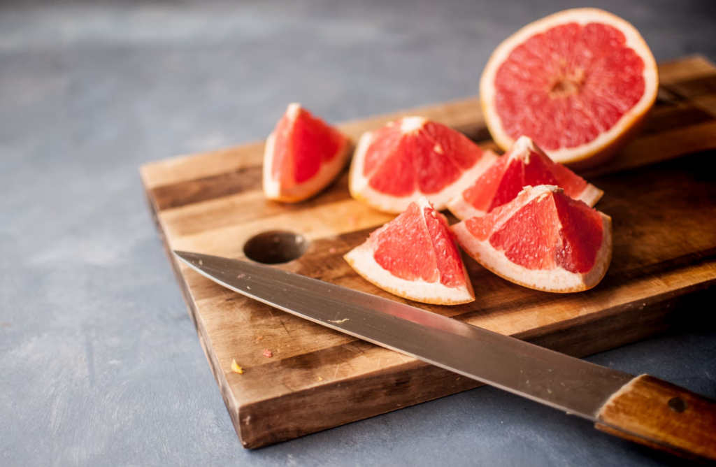 Close-up of a grapefruit on a cutting board next to a knife, highlighting its potential interactions with various medications. The vibrant fruit serves as a reminder to be cautious about food and medication interactions, especially for individuals over 60.