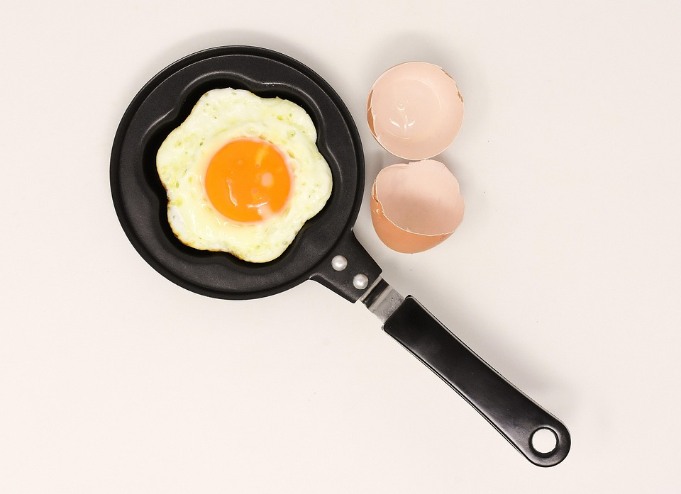 An egg frying in a pan on a white surface, emphasizing the importance of food safety for older adults and highlighting foods to avoid after 60 to prevent foodborne illnesses.