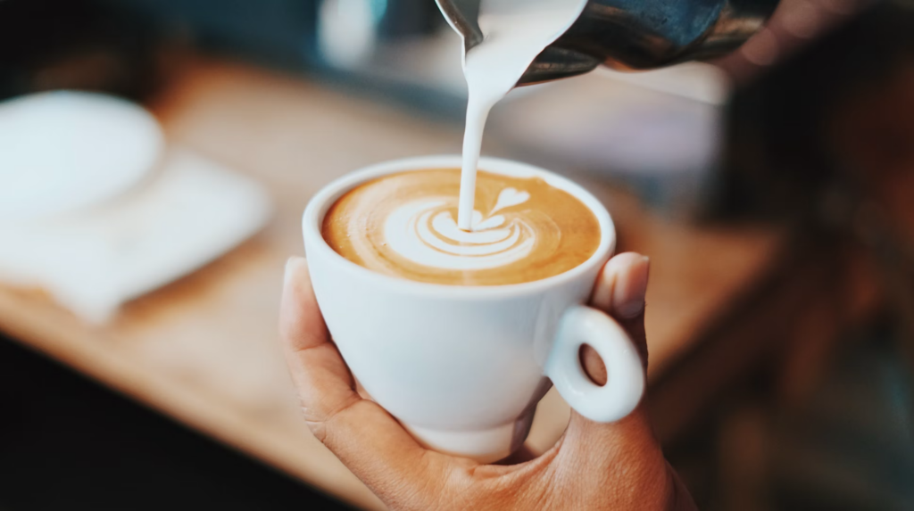 A person holding a cup of coffee featuring intricate latte art, reflecting a moment of enjoyment and relaxation, while keeping in mind foods to avoid after 60 for optimal health.