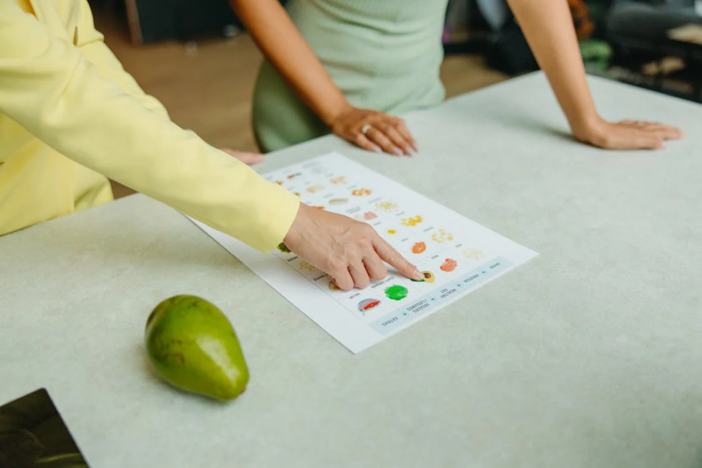 Two women analyzing a nutritional chart on a page, surrounded by various fruits.