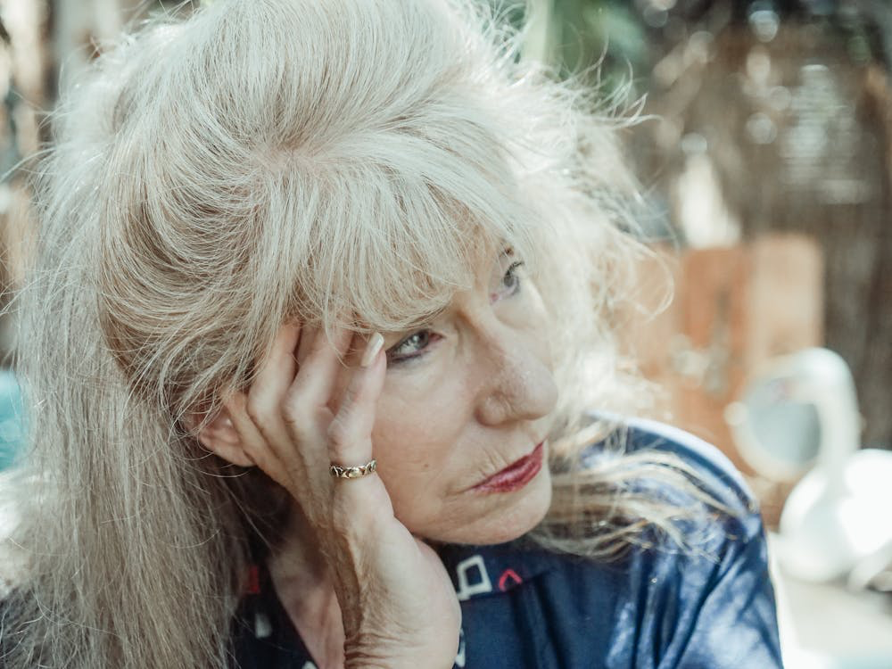 A woman with long white hair sits on a bench, her expression reflecting the early signs of dementia.