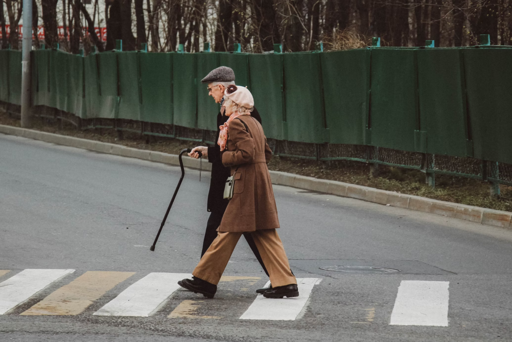 An elderly couple holding hands as they carefully cross the street together, smiling and enjoying their time.