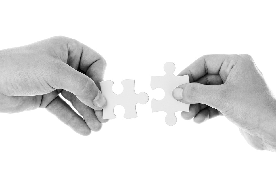 Two hands gently fitting a puzzle piece together, on a white background.