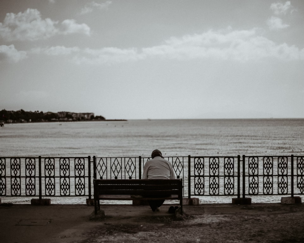 A person sits quietly on a bench by the ocean, gazing at the waves, lost in thought and memories.